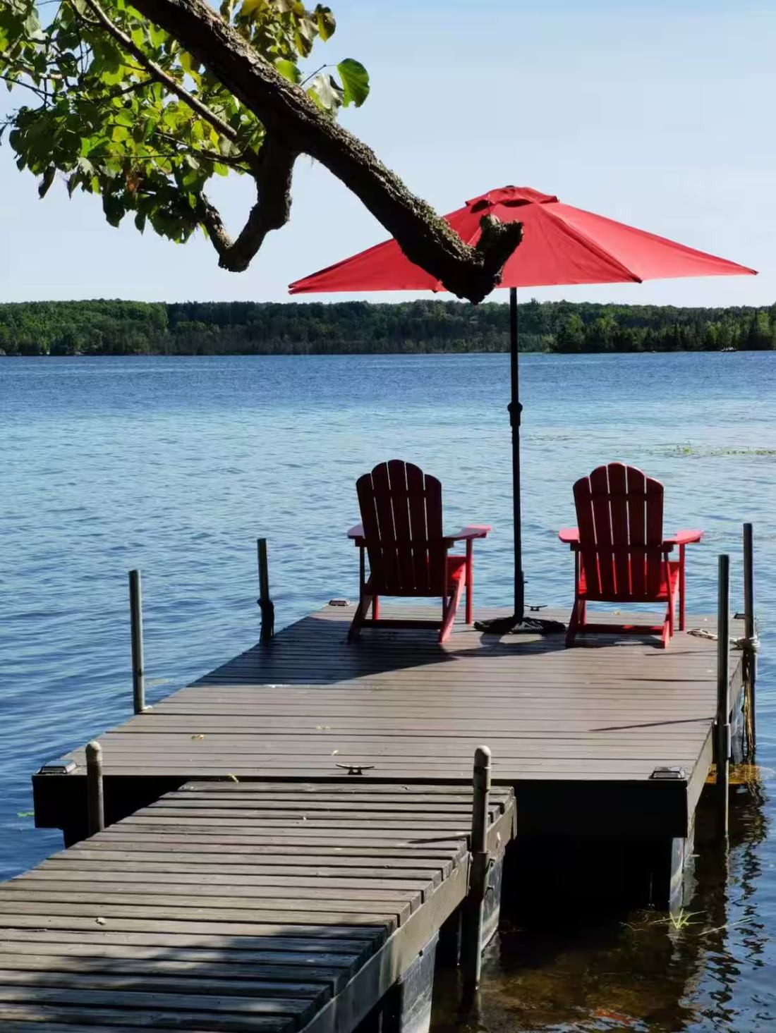 Dock with two red Adirondack chairs and a red umbrella over the lake